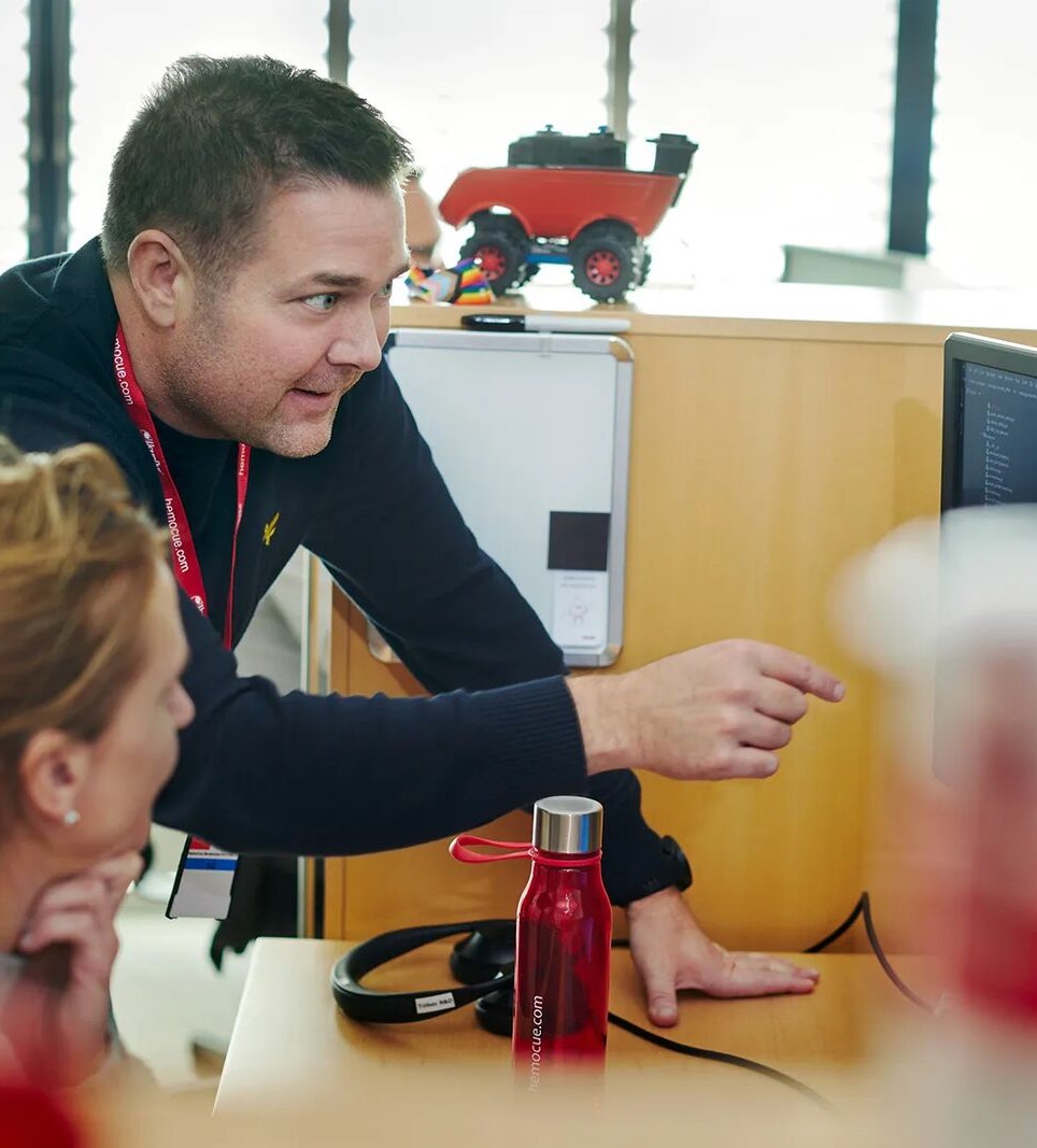 Male HemoCue employee helping colleague at a computer