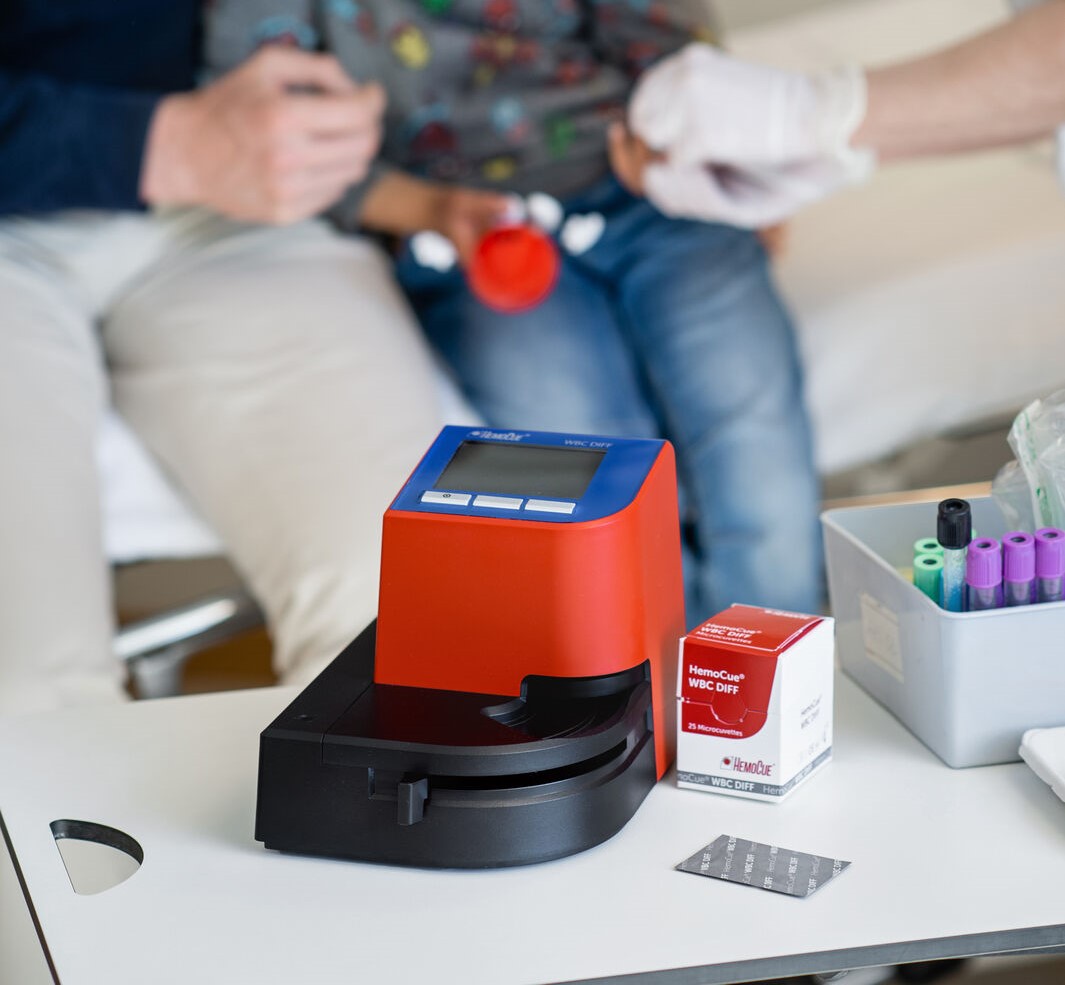 A HemoCue WBC DIFF System with a father and child at a hospital sitting on a bed