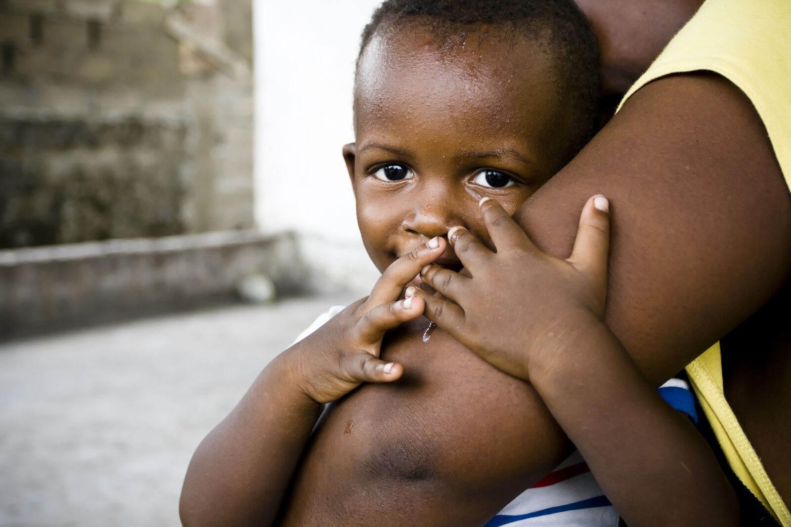 Small African boy hugging mothers arm